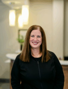 Smiling female dental professional in a black jacket, set against a bright, welcoming dental office background, representing the team at Progressive Dental Care.