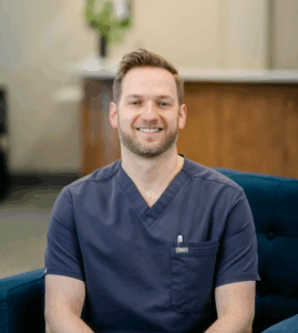 Dr. Edward "Ned" Gold, smiling in dental scrubs, seated in a welcoming office environment at Progressive Dental Care, representing the dedicated dental team.