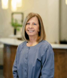 Dental assistant at Progressive Dental Care smiling in professional attire, with a welcoming reception area in the background.
